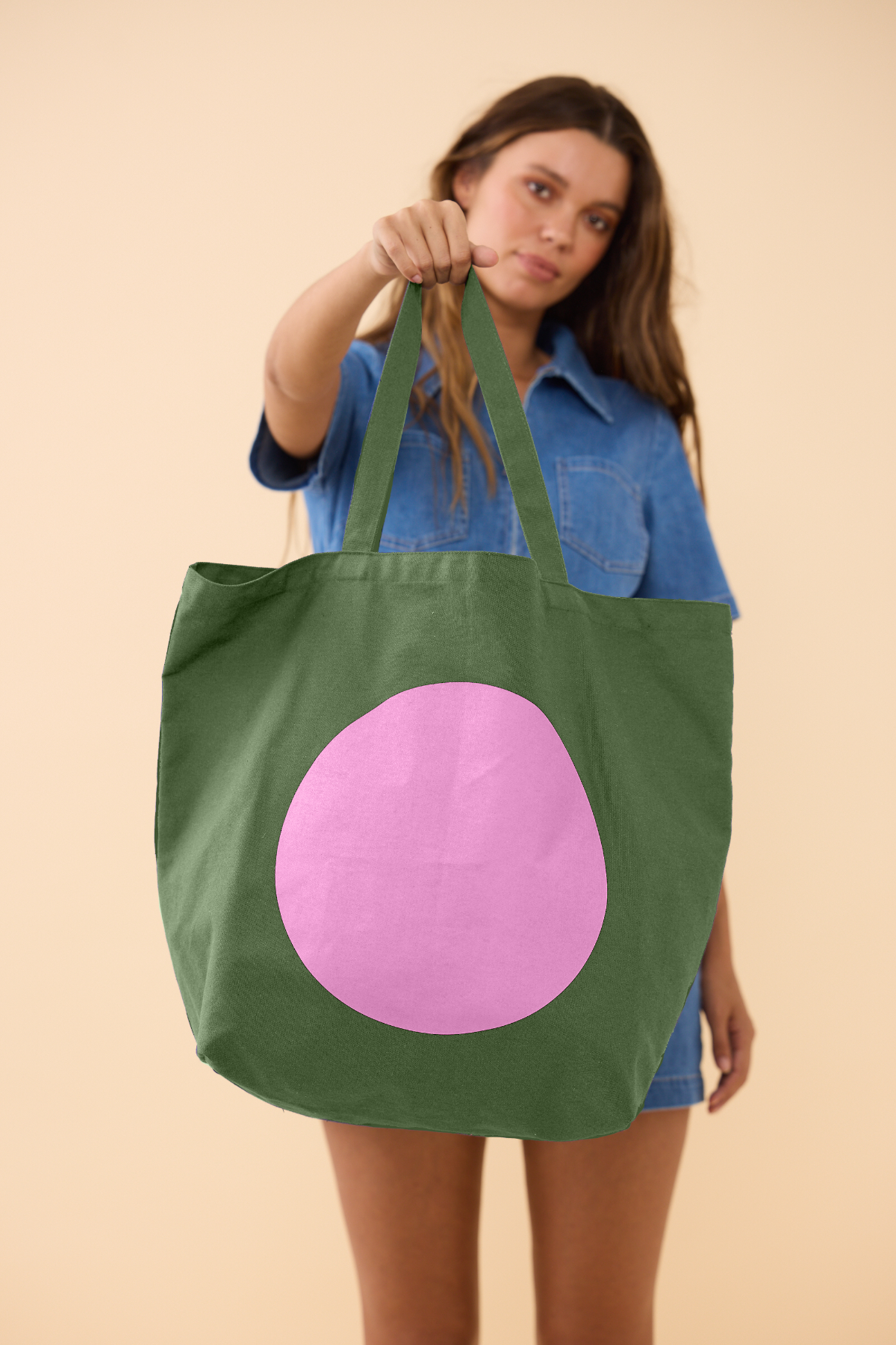 Woman holding a green tote bag with a pink circle on a beige background
