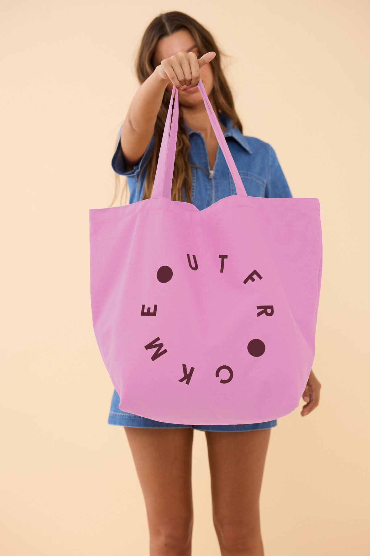 Person holding a pink tote bag with text against a beige background