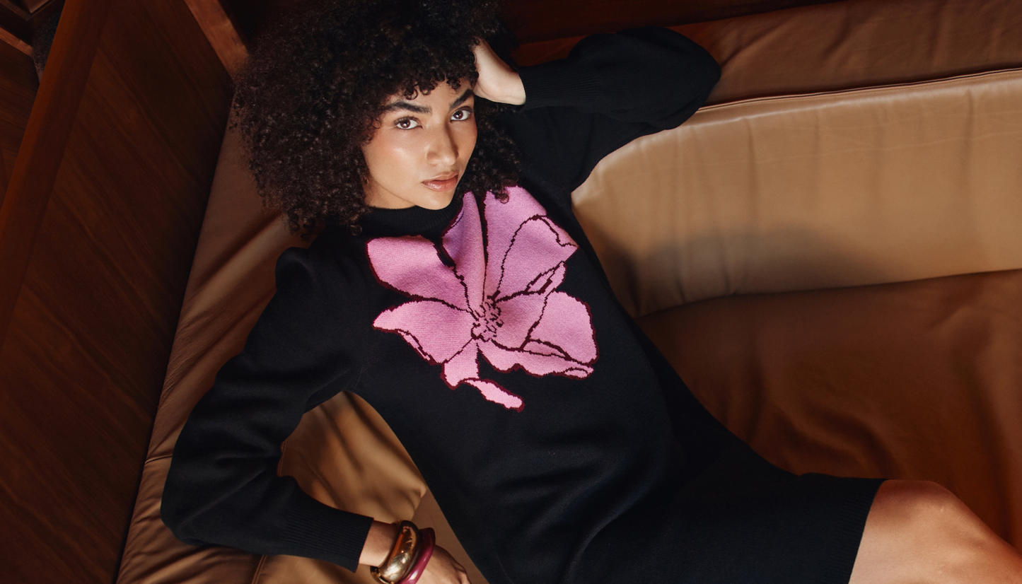 Person wearing a black sweater with a pink floral design, sitting on a brown couch.