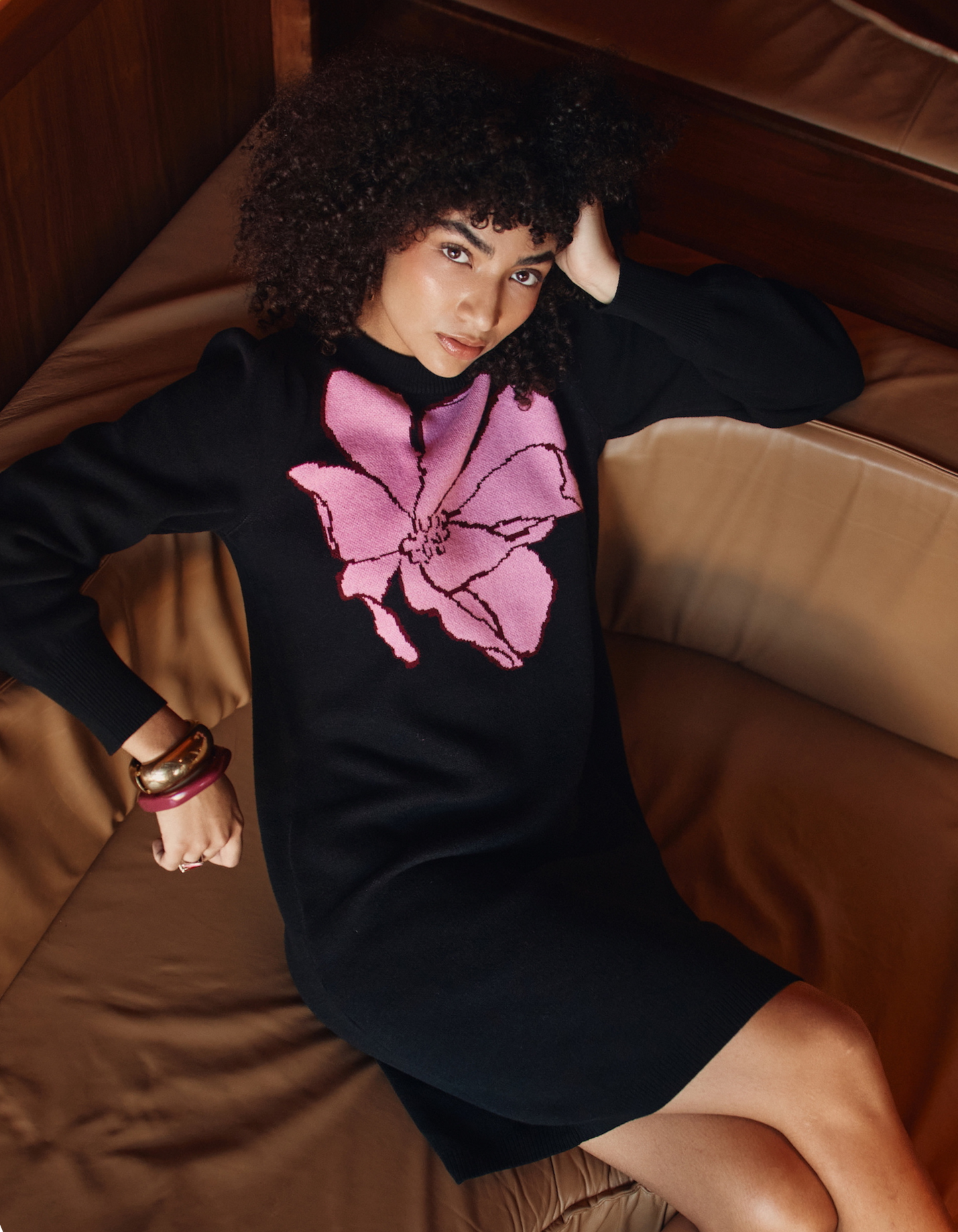 Woman wearing a black sweater with a pink floral design, sitting on a brown couch.