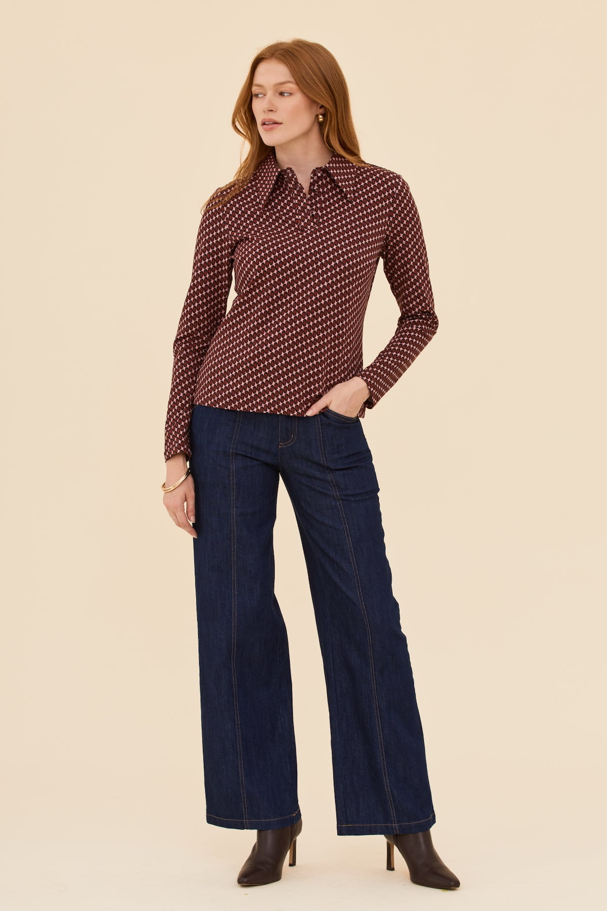 Woman wearing a patterned blouse and dark blue flared pants on a beige background