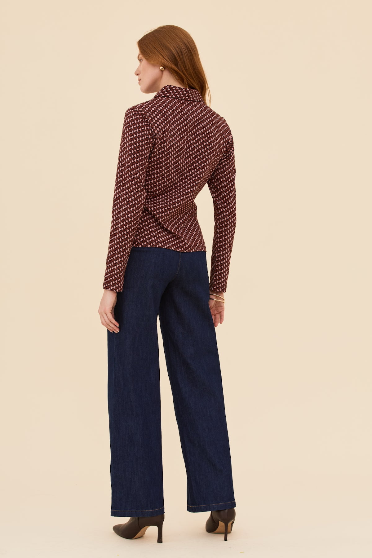 Woman wearing a patterned blouse and dark blue pants on a beige background