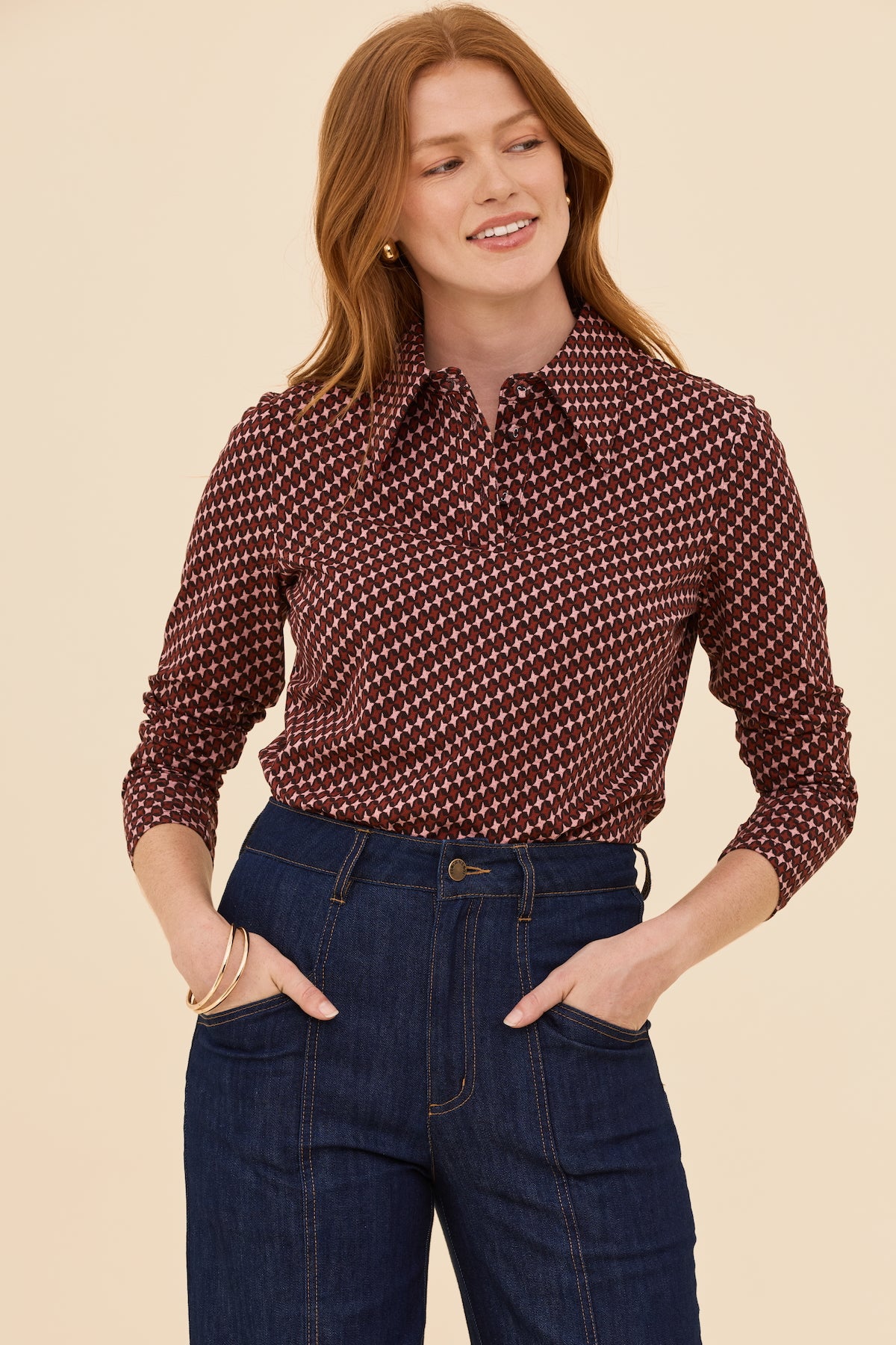 Woman wearing a patterned blouse and jeans against a beige background