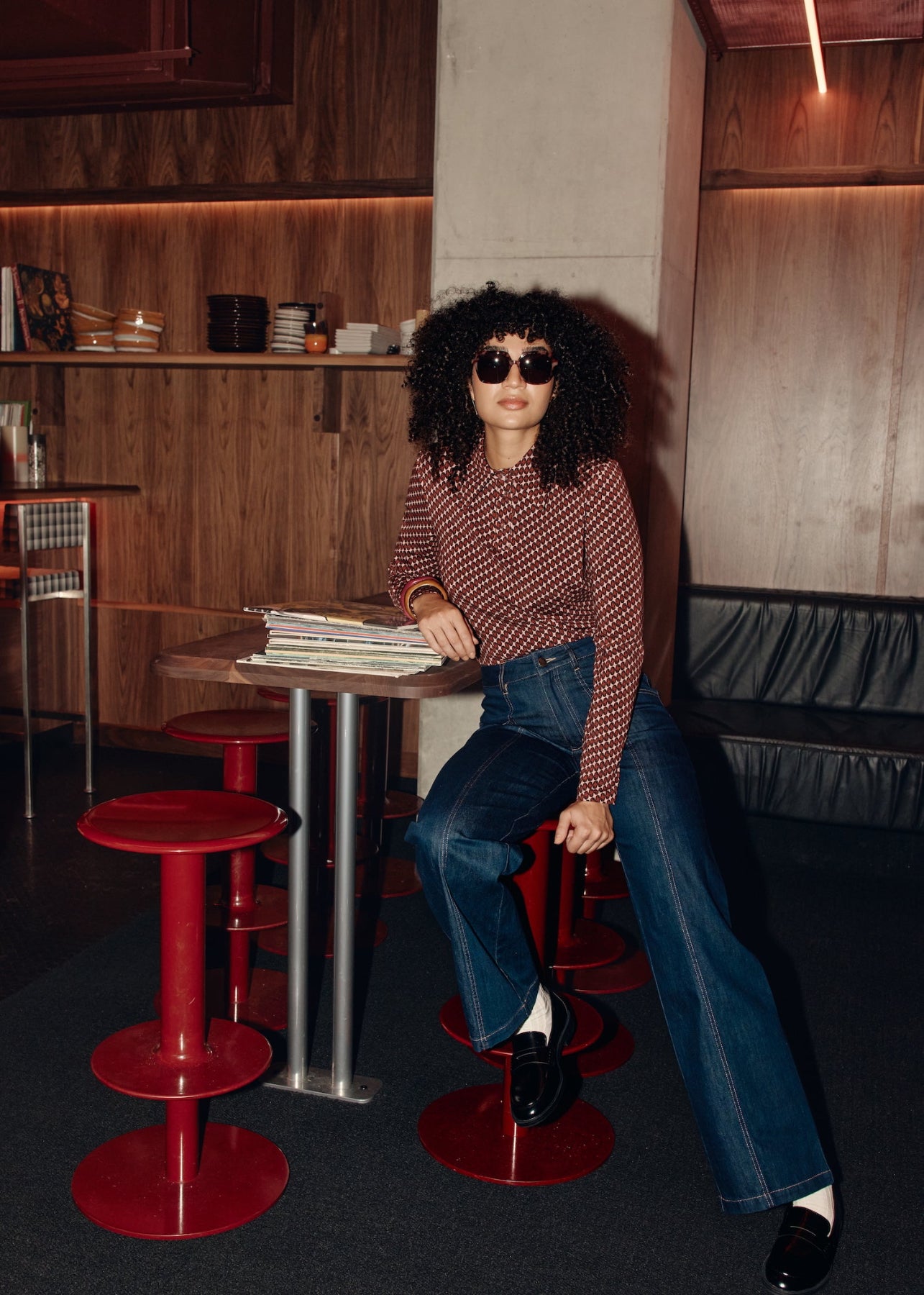 Woman sitting at a table in a modern cafe with red stools and wooden walls.