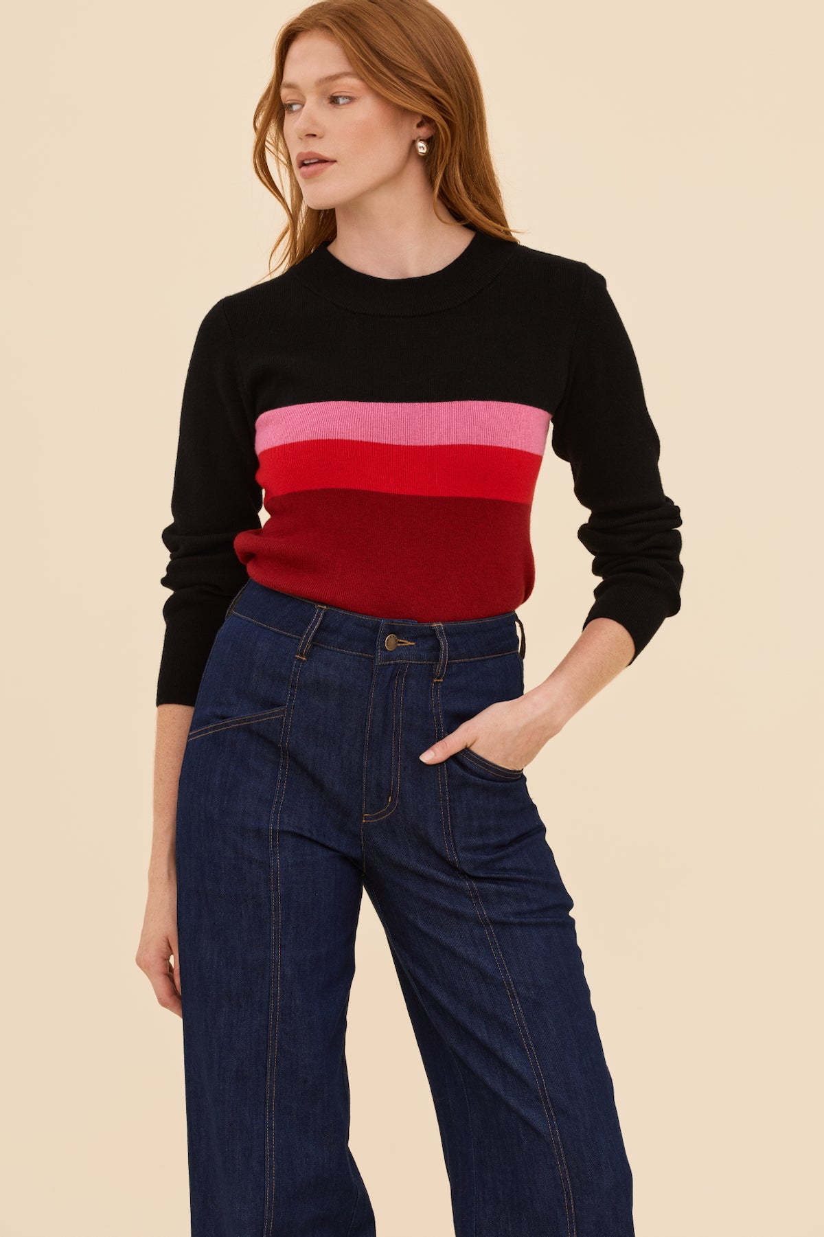 Woman wearing a black sweater with red and pink horizontal stripes and blue jeans on a beige background