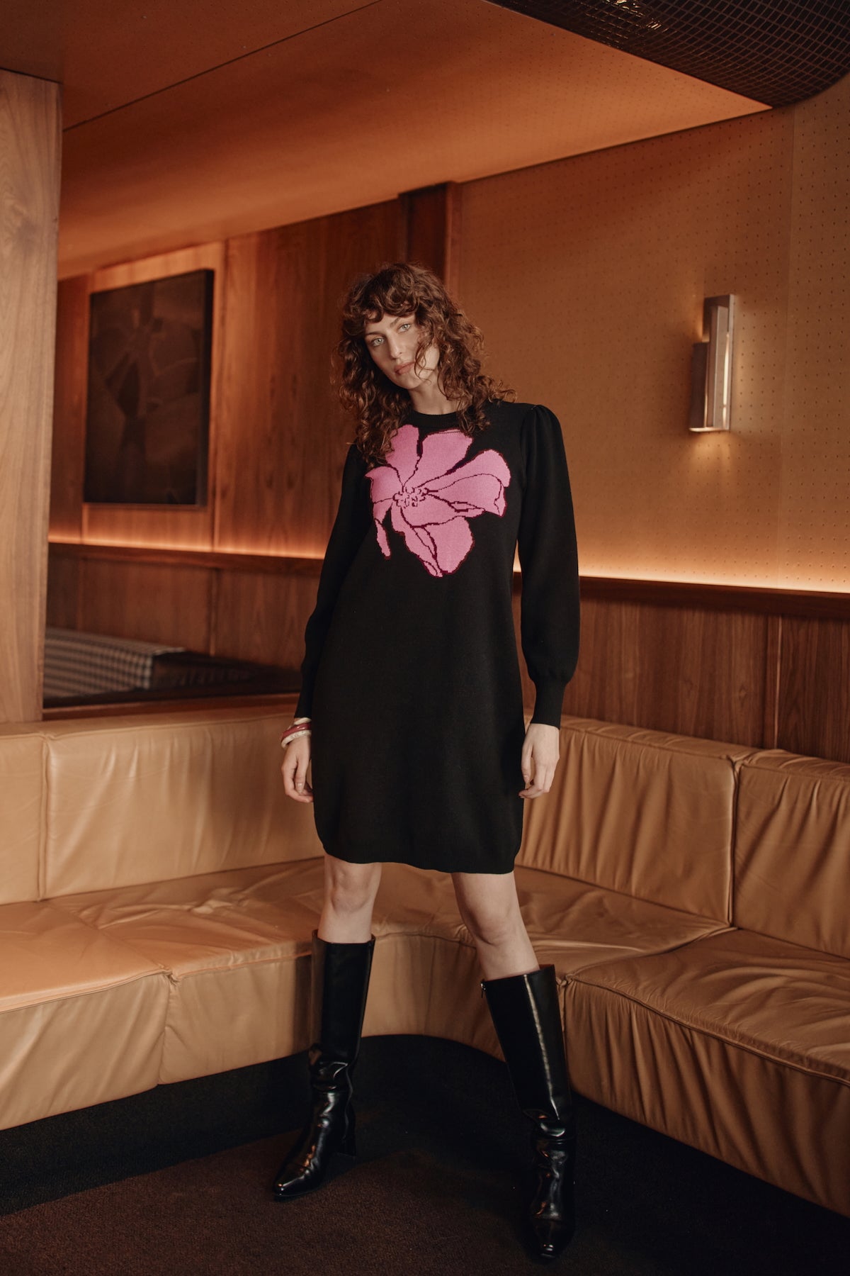 Person wearing a black dress with a pink flower design in a room with wooden walls and a brown couch.