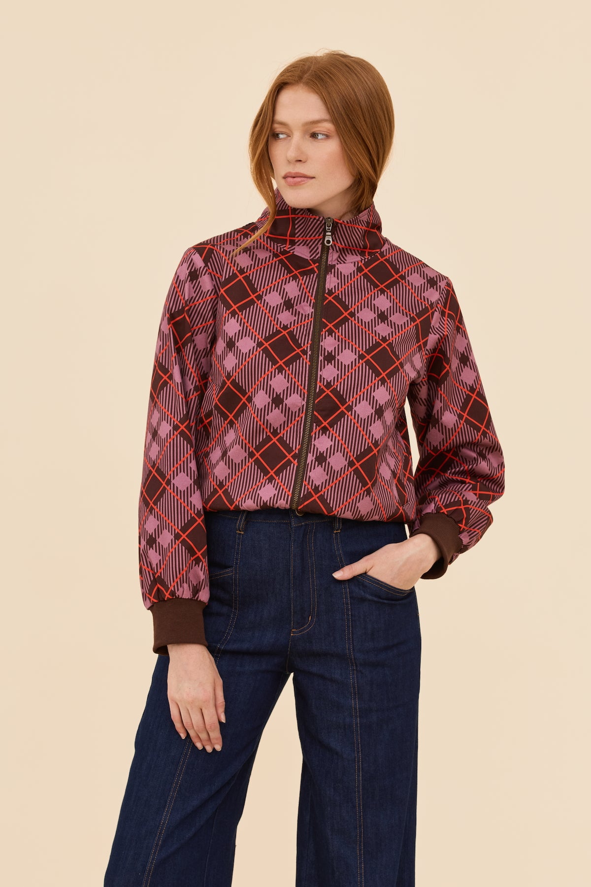 Woman wearing a plaid bomber jacket and dark jeans on a beige background