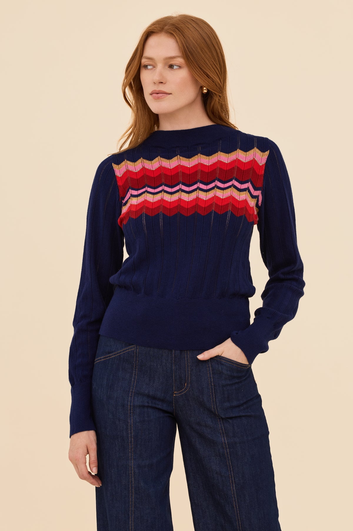 Woman wearing a navy pointelle sweater with colorful pattern on a beige background